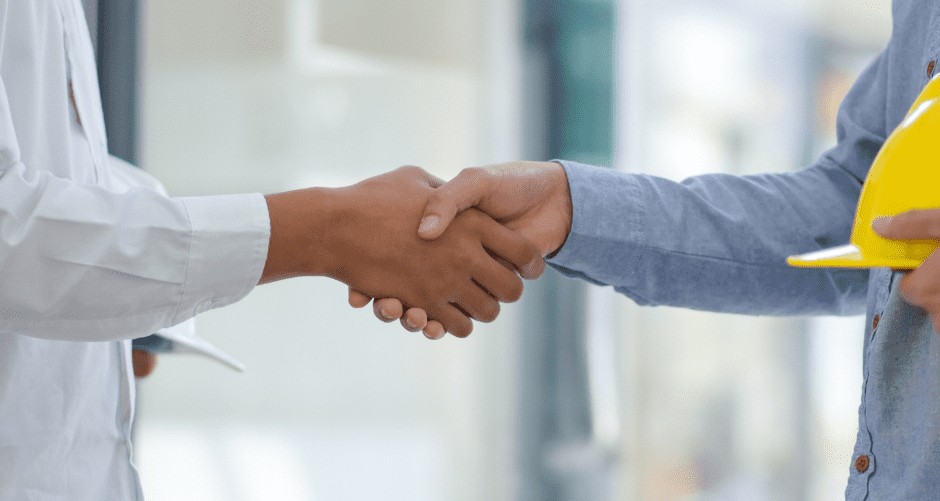 A homeowner and a contractor holding a hard hat shaking hands